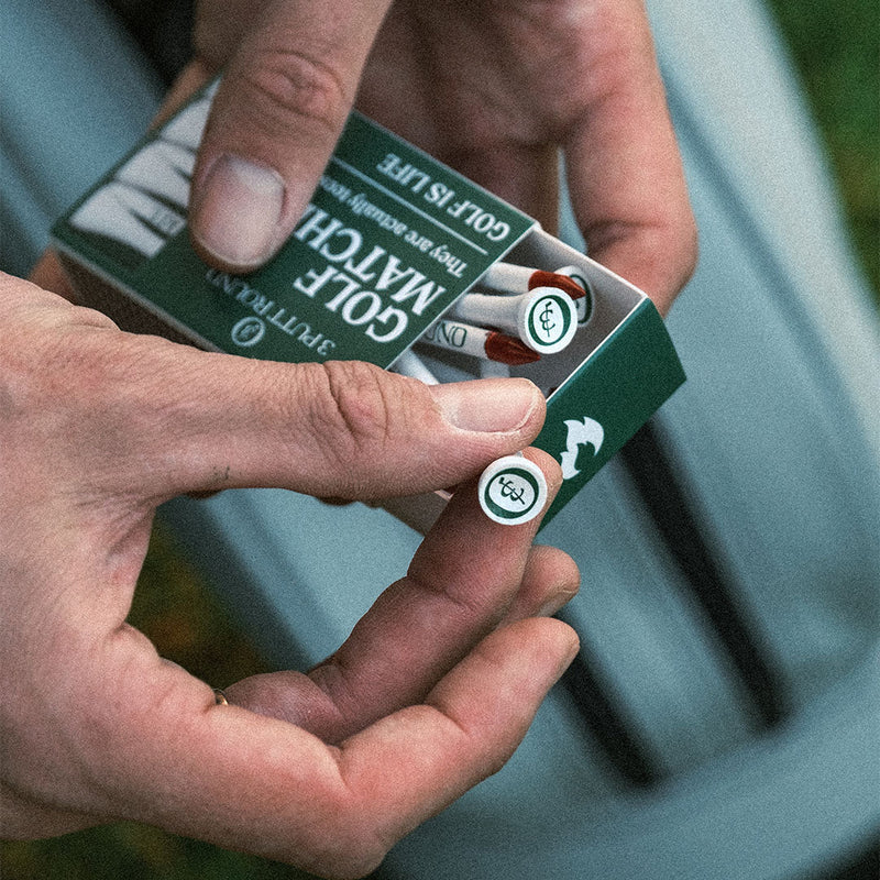 Green golf tees from the Three Putt Round matchbox, neatly arranged in a compact box for easy use on the golf course.