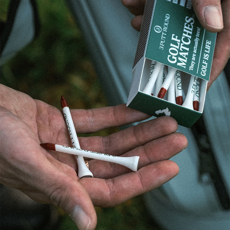 Green golf tee match box by Three Putt Round showing a wooden golf tee inside a compact, green-colored matchbox.